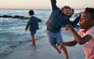 Kids jumping in the water's edge at sunset